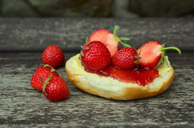 Fresh strawberries on buttered bread with strawberry jam placed on wooden table. Can be used for food blogs, breakfast menu designs, health and nutrition articles, or dessert recipes.