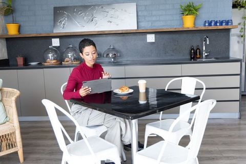 African american woman working on tablet in modern kitchen cafe with coffee and pastry