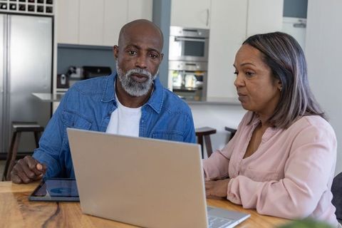 Senior African American Couple Discussing Finances on Laptop at Kitchen Table, Focused