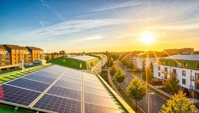 Solar panels on green rooftop capturing sunrise over modern eco-friendly neighborhood cityscape
