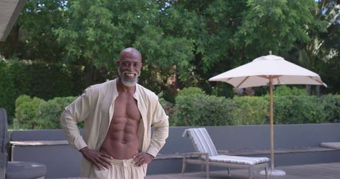 Sunlit senior african american man posing on deck in open shirt showing sculpted abs and relaxed smi