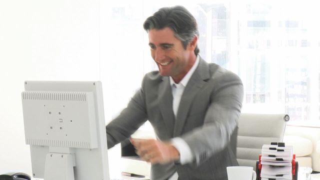 Businessman in grey suit celebrating at office desk, suitable for business success, corporate achievements, workplace motivation, modern office settings, career growth themes.