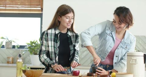 Female Friends Cooking Together in Bright Kitchen Chopping Fruit and Grinding Herbs