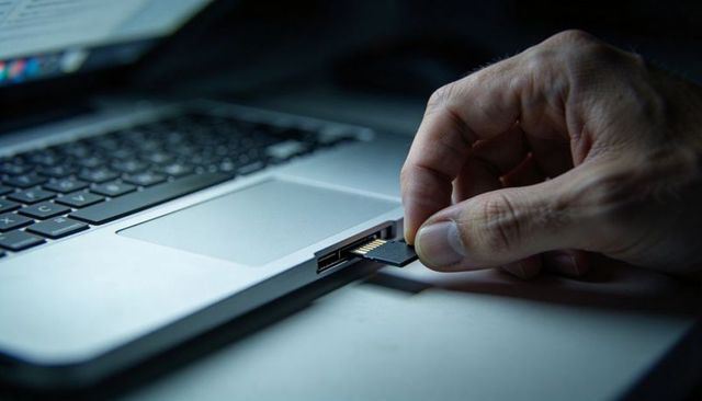 Right hand inserting microsd adapter into laptop card slot on modern desk