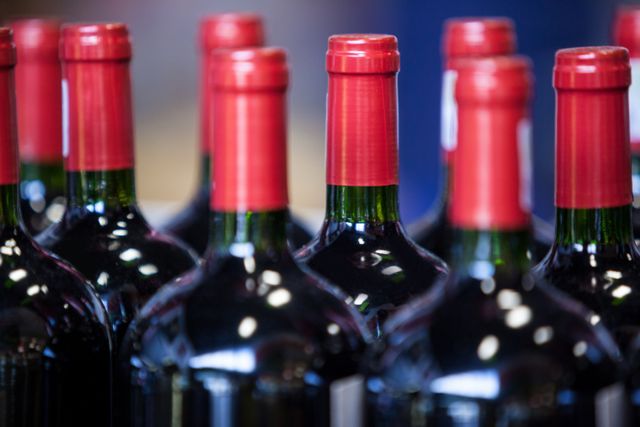 Close-up view of multiple wine bottles with red caps arranged in a supermarket. Ideal for use in articles or advertisements related to wine, retail shopping, alcohol sales, or product packaging. Can be used to illustrate concepts of wine selection, shopping experiences, or retail displays.