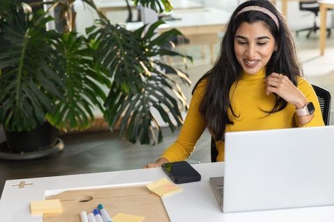 Indian professional woman working on laptop at modern sunlit open-plan office desk