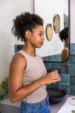 African american woman applying moisturizer at modern bathroom vanity, natural skincare
