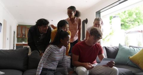 Multiethnic friends gathered reading letter on gray sectional sofa in bright living room