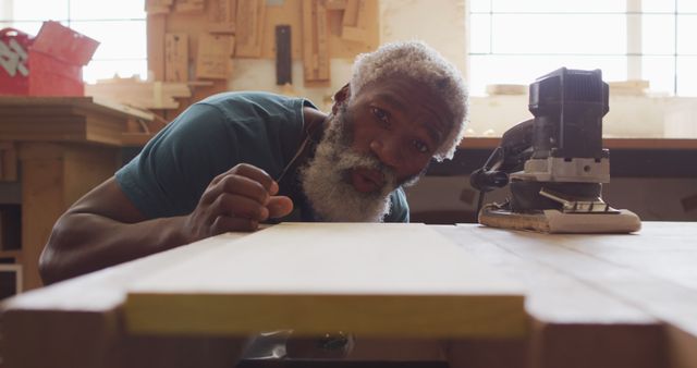 African american male carpenter blowing the dust over wooden plank at a carpentry shop - Download Free Stock Photos Pikwizard.com