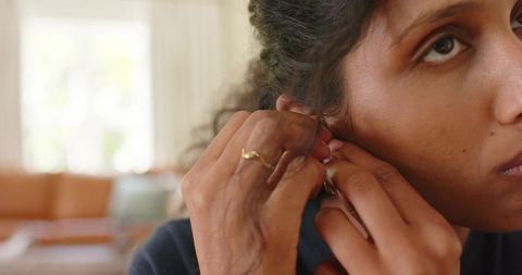 African woman adjusting gold hoop earring in sunlit living room, closeup portrait