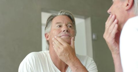 Mature man checking stubble in mirror while grooming at bathroom vanity, reflective moment
