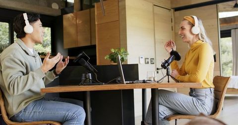 Two hosts recording podcast conversation in minimalist wood home studio with headphones