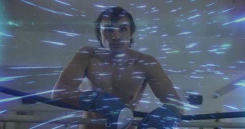Shirtless boxer leaning on ropes wearing gloves facing camera with blue light streaks