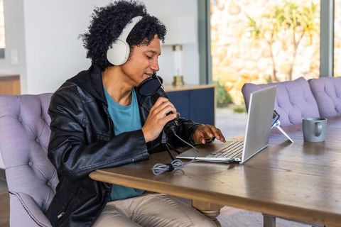 African american man recording podcast at home with laptop and microphone