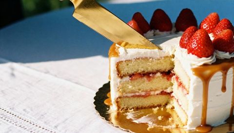 Cutting strawberry caramel layer cake with gold knife, dripping frosting and berries