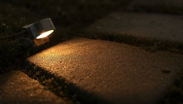 Amber spotlight illuminating damp concrete paver on garden path at night close-up texture