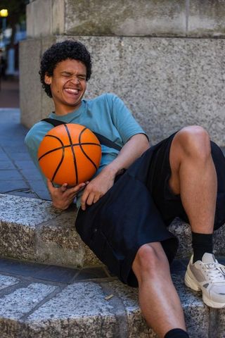 Laughing african american man holding basketball, relaxing on urban stone steps, casual