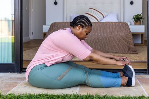 African american woman stretching on patio threshold during home workout in athleisure