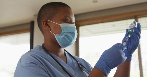 Nurse preparing covid-19 vaccine dose in clinic wearing mask, gloves and stethoscope