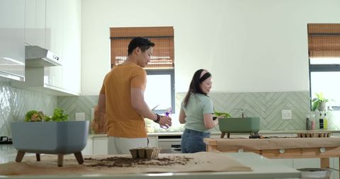 Couple potting indoor plants on bright modern kitchen counter with scattered potting soil