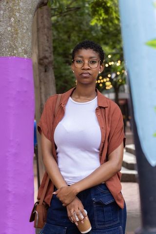 Confident african american woman standing in urban plaza holding coffee, casual style
