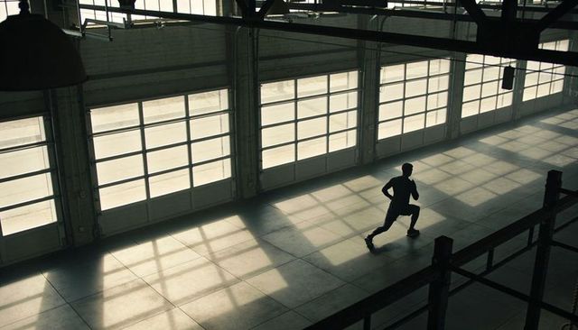 Athlete Lunging Through Sunlit Industrial Warehouse with Dramatic Shadow Grid