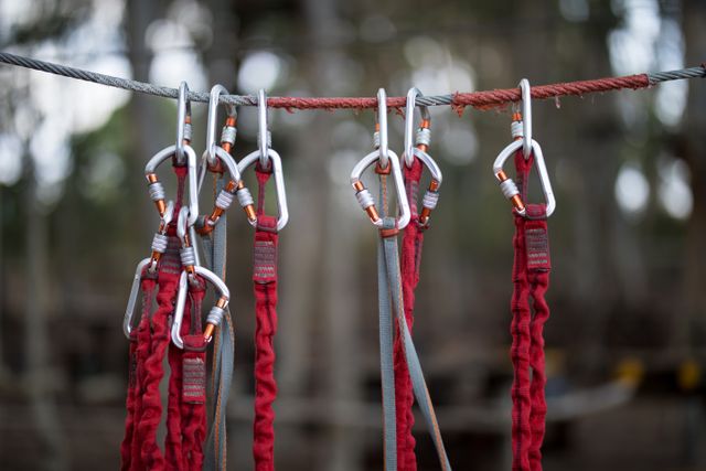 Carabiners hanging on a wire rope with red straps in an outdoor park. Ideal for illustrating adventure parks, climbing safety, outdoor activities, and recreational equipment. Useful for blogs, articles, and advertisements related to outdoor sports and safety gear.