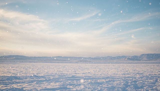 Endless snow plain stretching over rippled drifts with falling snow and mountain horizon