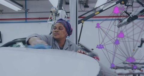 Woman technician wiping car roof while robotic network overlay highlights modern auto shop