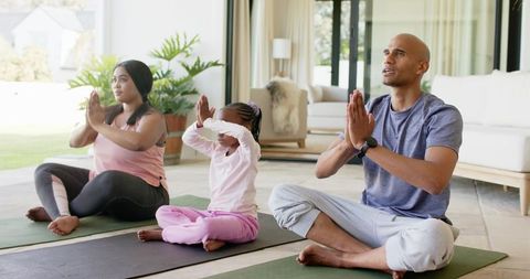 Multiracial family meditating together on sunlit living room yoga mats for wellness