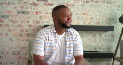 African american man sitting in modern living room chair looking thoughtfully to right