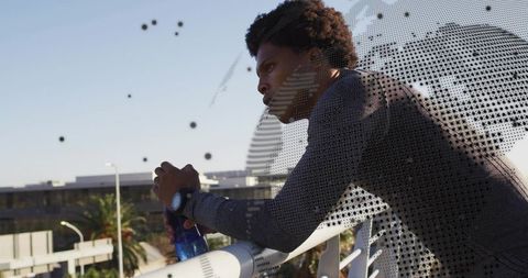 Leaning urban athlete contemplating city skyline with smartwatch and blue water bottle
