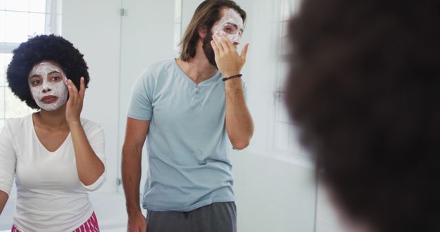 Image shows a couple in a modern bathroom applying face masks. They are engaging in a skincare routine together and enjoying a moment of bonding. The scene implies self-care and relaxation, making it ideal for use in articles or advertisements related to beauty, health, wellness, and relationship bonding.