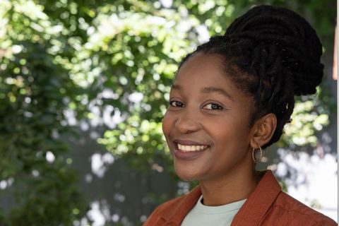 Smiling woman standing in sunlit garden wearing rust jacket and hoop earring