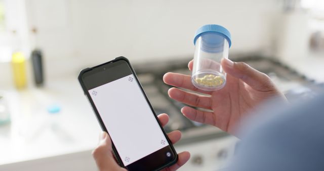 Person uses smartphone to scan and fill a prescription container in a kitchen. Suitable for technology in healthcare themes, digital medication tracking, and modern healthcare innovations.