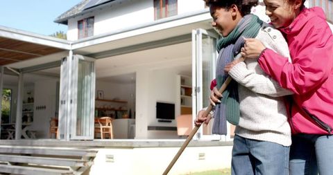 Mother and son enjoying outdoor fun raking leaves in fall garden