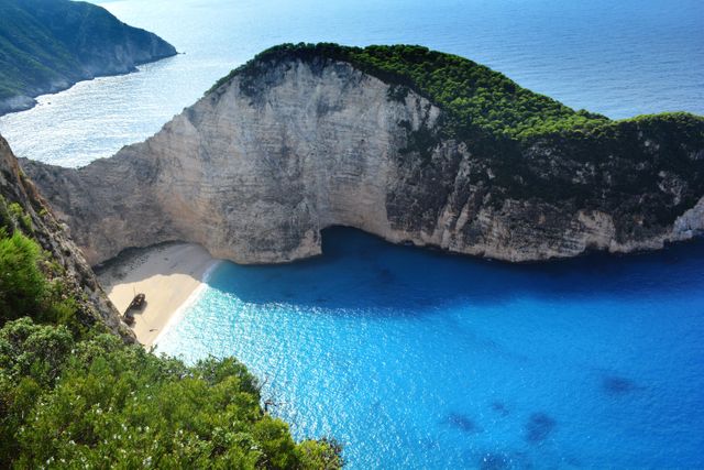 This aerial view showcases the stunning Navagio Beach on Zakynthos Island, Greece, renowned for its crystal-clear turquoise waters, dramatic cliffs, and the iconic shipwreck on the sandy beach. Perfect for use in travel articles, tourism promotions, nature and adventure publications, and Mediterranean vacation planning materials.