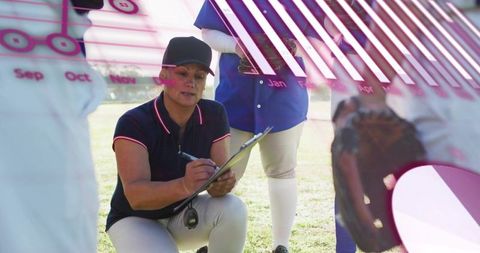 Female softball coach kneeling writing clipboard coaching team strategy analytics overlay