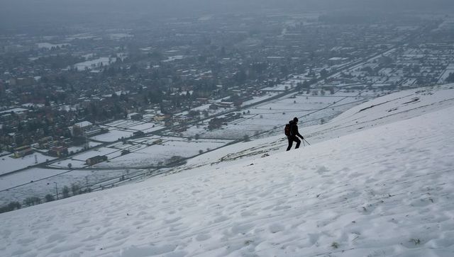 Solitary hiker ascending snowy hillside above foggy rural valley with panoramic winter view