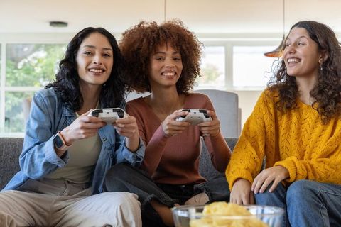 Diverse young women playing video games on couch laughing and holding controllers