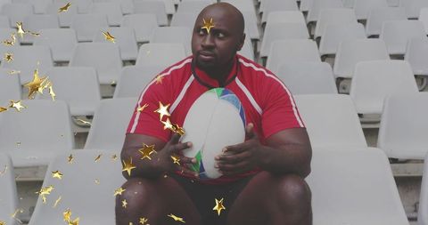 Solitary rugby player holding colorful ball on empty stadium seats with gold star confetti