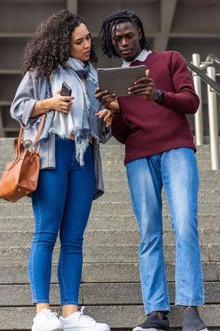 Young professionals collaborating on tablet on city steps, sharing ideas while checking device