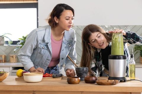 Woman and teen preparing green smoothie together at kitchen island