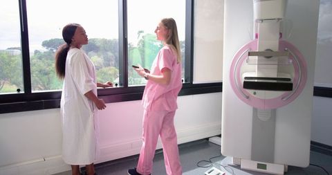 Mammography consultation showing patient in gown with clinician in pink scrubs by window