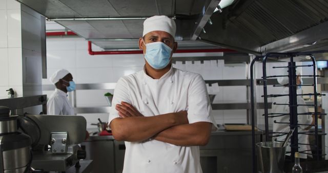 Image depicts a professional chef in a commercial kitchen, wearing a medical mask and a white chef uniform. Ideal for use in articles and content related to culinary arts, workplace safety, health precautions in food preparation, and professional kitchens.