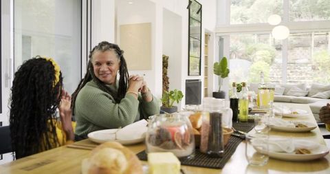 Sunlit multi-generational Black family sharing meal at long wooden dining table together