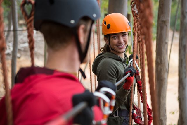 Smiling young woman looking at man while crossing zip line in the forest