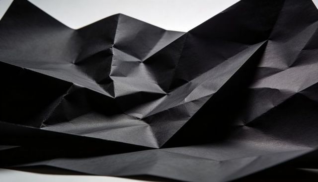 Crumpled black paper abstract texture with sharp folds, creases and matte highlights