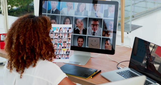 Recruiter sitting in workspace conducting a virtual interview with multiple candidates displayed on the computer screen while holding a profile sheet with applicant photos. Ideal for illustrating remote hiring processes, online interviews, HR technology solutions, and diverse talent acquisition.