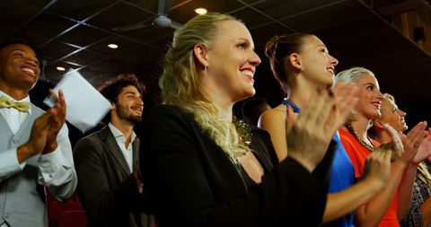 a diverse group of young adults is enthusiastically applauding at an event, indicating they are enjoying a captivating performance or speech. this image can be used for marketing materials, event promotions, or any context where audience engagement is a key focus. it conveys energy, excitement, and approval, making it ideal for showcasing participation, celebration, or even conference or awards settings.